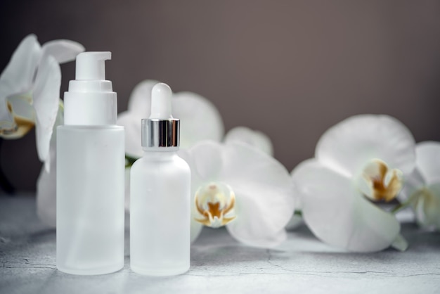 Witte glazen serumfles, lotionpompfles en zalfpotmodellen in de badkamer met orchideebloemen op de achtergrond, merkloze cosmetische producten, spa-cosmetisch product-brandingmodel