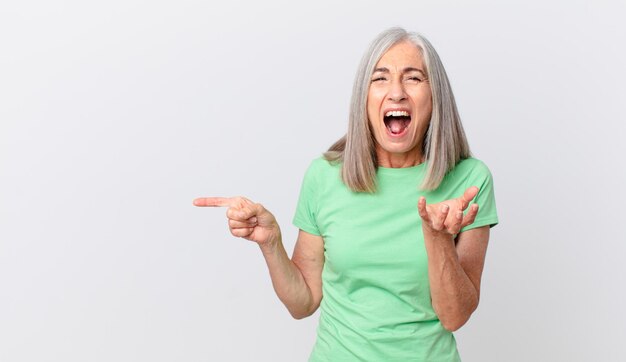 Witte haarvrouw van middelbare leeftijd die boos, geïrriteerd en gefrustreerd kijkt en naar de zijkant wijst