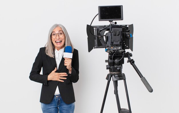 Witte haarvrouw van middelbare leeftijd die hardop lacht om een hilarische grap en een microfoon vasthoudt. tv-presentator concept