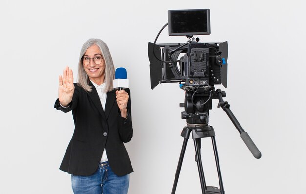 Witte haarvrouw van middelbare leeftijd die lacht en er vriendelijk uitziet, nummer vier toont en een microfoon vasthoudt. tv-presentator concept