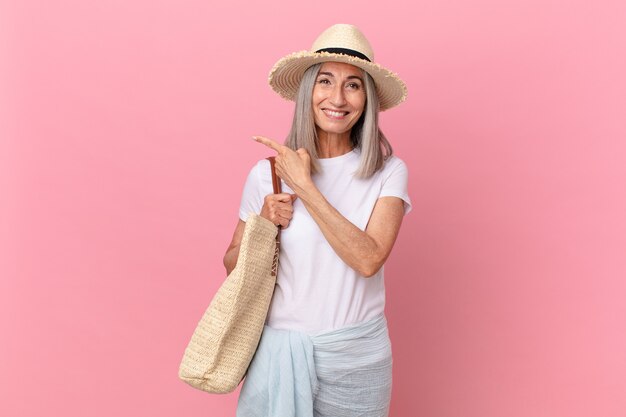 Witte haarvrouw van middelbare leeftijd die vrolijk lacht, zich gelukkig voelt en naar de zijkant wijst. zomer concept