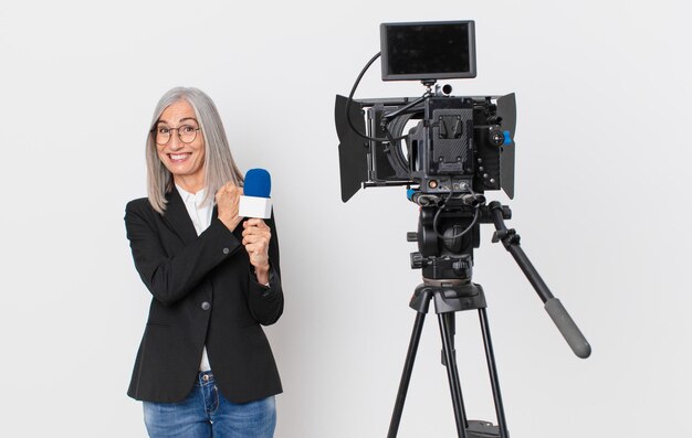 Witte haarvrouw van middelbare leeftijd die zich gelukkig voelt en een uitdaging aangaat of een microfoon viert en vasthoudt. tv-presentator concept