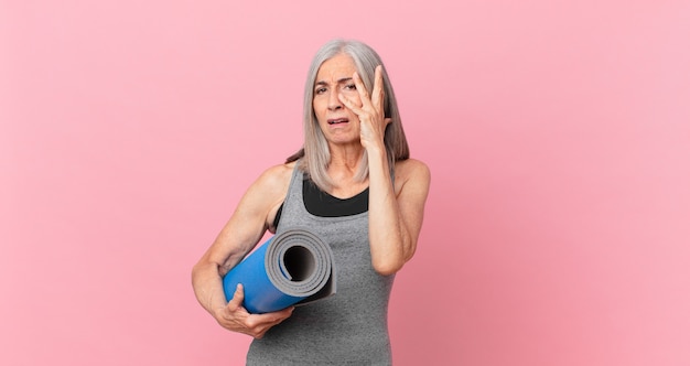 Witte haarvrouw van middelbare leeftijd die zich verveeld, gefrustreerd en slaperig voelt na een vermoeiende en een yogamat vast te houden. fitnessconcept