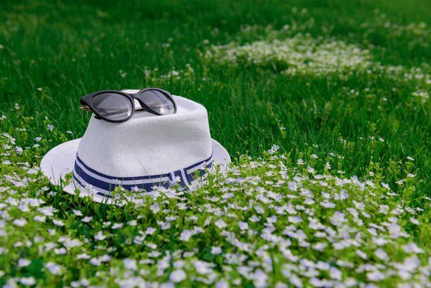 Witte hoed en zonnebril op groen gras en Lentebloemen, natuurlijke achtergrond voor recreatie, vakanties