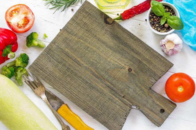 Witte houten keukenachtergrond Snijplank en verse groenten, olijfolie en kruiden bovenaanzicht