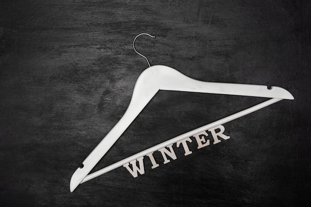 Witte houten kleerhanger en inscriptie winter, zwart oppervlak. wintercollectie kleding.