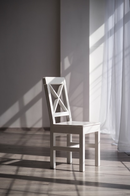 Witte houten stoel tegen de achtergrond van een mooie lichte ruime kamer met witte muren en licht parket in de ochtendzon