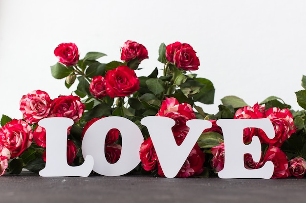 Witte inscriptie liefde tegen de achtergrond van rode rozen op beton