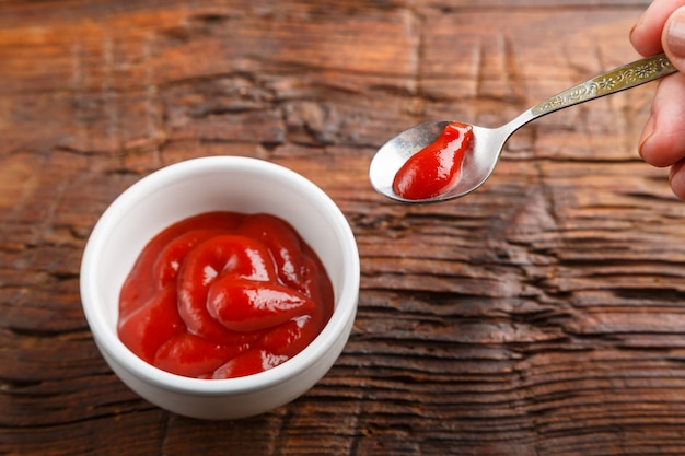 Witte juskom met ketchup en hand met een lepel saus op een houten tafel. Horizontale foto