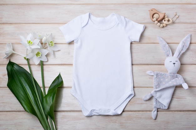 Witte katoenen romper met korte mouwen voor baby's met zacht lelieboeket, houten vogelspeelgoed en konijn. Ontwerp genderneutraal rompersjabloon, pasgeboren romper afdrukpresentatie mock-up