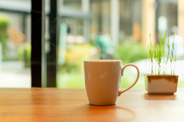 Witte keramiek koffiemok met rook en kleine plant op houten tafel in café.