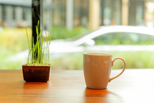 Witte keramiek koffiemok met rook en kleine plant op houten tafel in café.