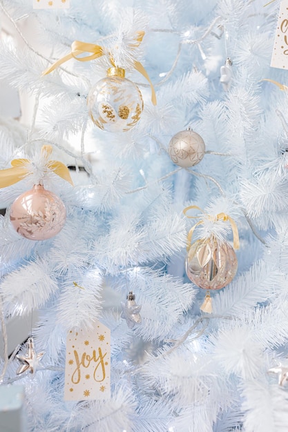 Witte kerstboom versierd met zilveren gouden roze kerstballen en prachtige glazen bollen op sprankelende en sprookjesachtige witte blauwe tak, decoratieve verlichting, kopieerruimte. Foto.