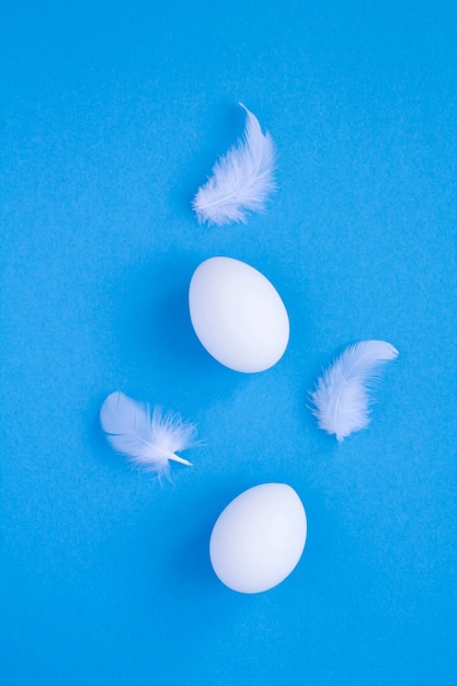 Foto witte kippeneieren en veren op het blauwe oppervlak. locatie verticaal.