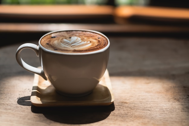 Witte koffiekop met latte kunst van de hartvorm op houten lijst