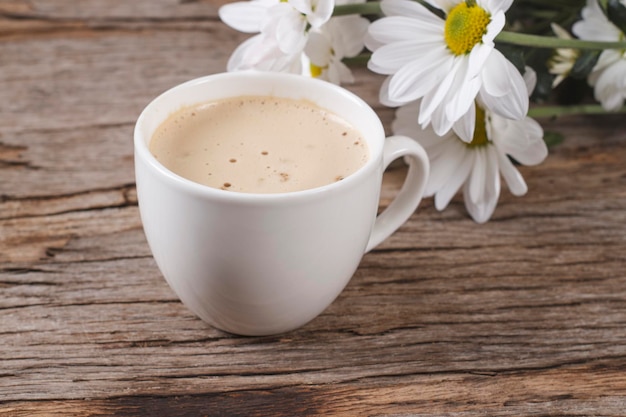 Witte koffiekop met warme cappuccino met latte op houten achtergrond met margrieten