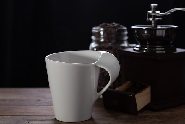 Witte koffiekopje, koffiemolen en geroosterde bonen op houten tafel met donkere achtergrond