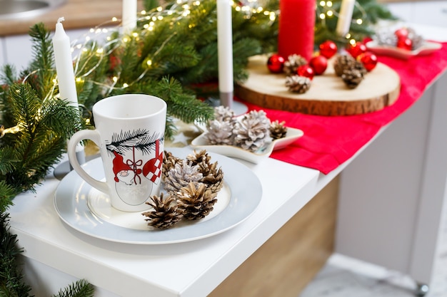 Witte koffiekopje op de keukentafel tegen de achtergrond van kerstversiering. Stukjes op een bord