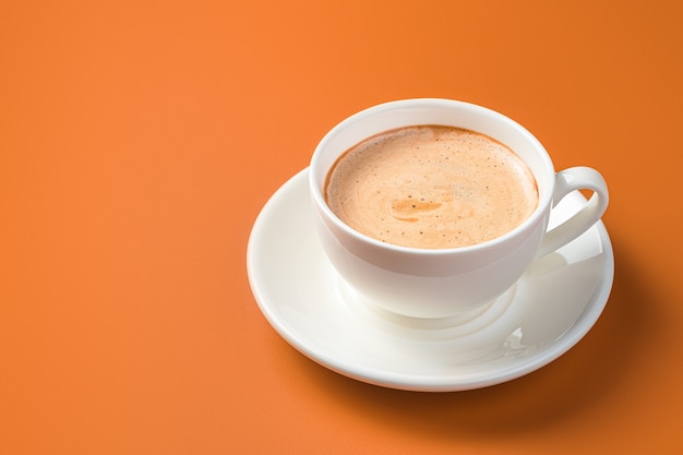 Witte koffiekopje op oranje muur met kopie ruimte. Zijaanzicht.