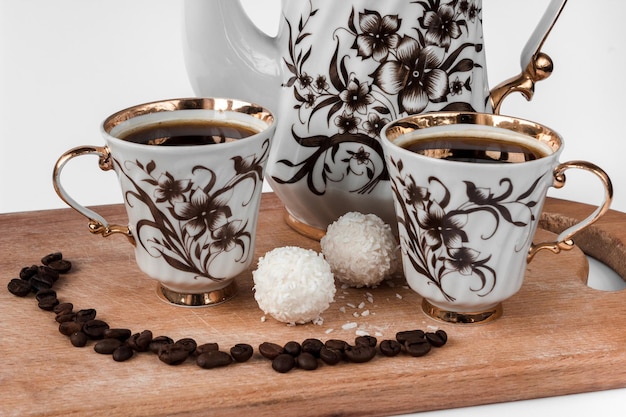 Witte koffiepot en twee kopjes koffie met granen en snoep op een houten plank close-up