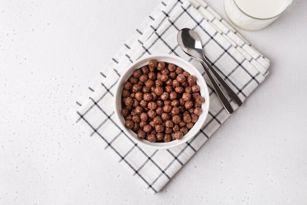 Witte kom met chocoladegranen op witte tafel Geserveerd met melk en lepels Ontbijt en begin van de dag