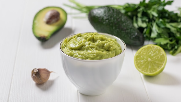 Witte kom met guacamole en avocado fruit op een witte houten tafel. dieet vegetarisch mexicaans eten avocado. rauw eten.