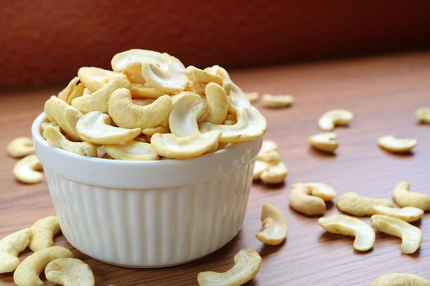 Witte kom vol gedroogde cashewnoten met wat kernels verspreid over houten tafel