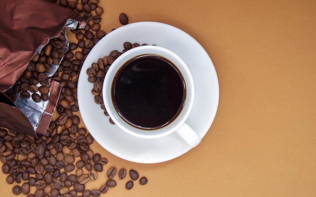 Witte kop Americano zwarte koffie zonder melk met een bos gebrande koffiebonen verspreid uit papieren verpakkingen. Koffie achtergrond, bovenaanzicht met kopie ruimte voor logo of tekst.