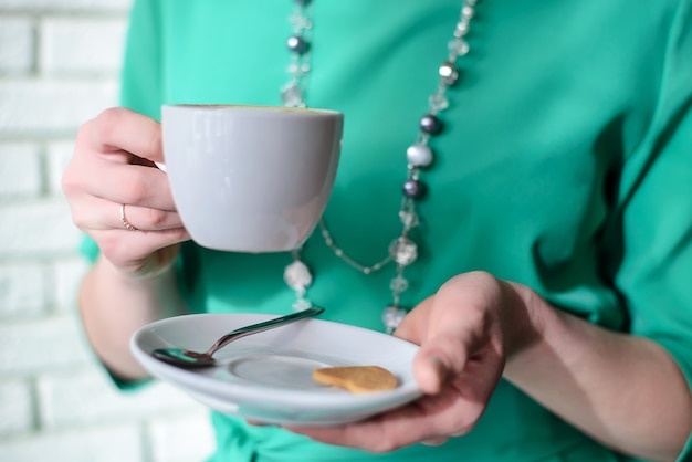 Witte kop en schotel met een drankje in de hand bij de vrouw in de groene jurk-closeup