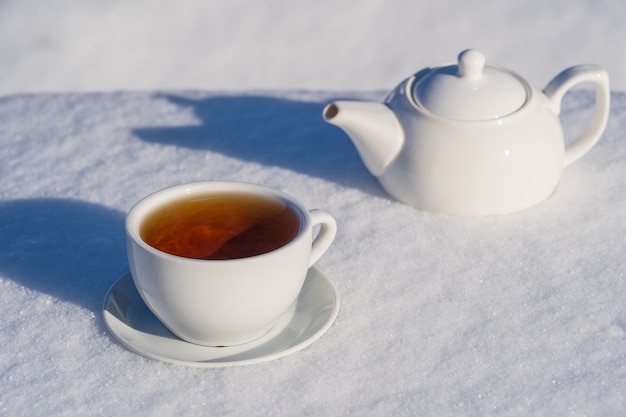 Witte kop hete thee en theepot op een bedje van sneeuw en witte achtergrond, close-up. Concept van kerst winterochtend