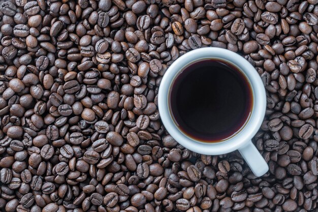Witte kop hete zwarte koffie met een achtergrond van vers gebrande koffiebonen close-up bovenaanzicht