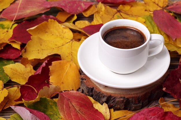 Witte kop koffie en herfstgele bladeren rond op houten tafel in de herfst.