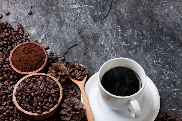 Foto witte kop koffie, koffiebonen in houten beker, houten lepel op zwarte steen