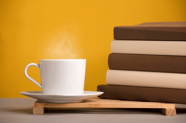 witte kop koffie met hete stoom op het bureau met bruine boeken geelachtig oranje achtergrond