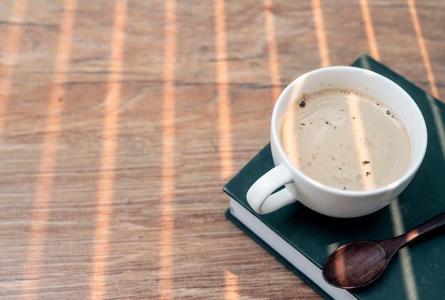 Witte kop koffie met houten lepel op groen boek op houten lijst.