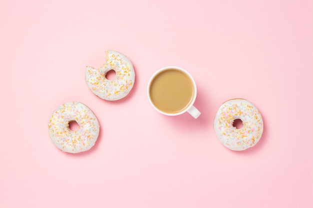 Witte kop, koffie of thee met melk en verse smakelijke zoete donuts op een roze achtergrond. Bakkerijconcept, vers gebak, heerlijk ontbijt, fast food.