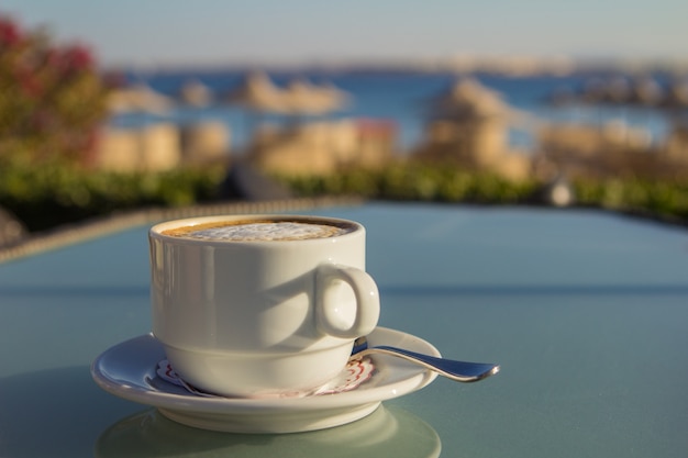 Witte kop koffie op de tafel op zee. Zomervakantie concept