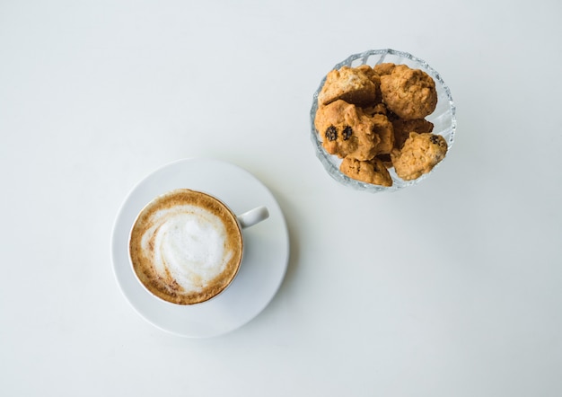 Witte kop met cappuccino en koekje op witte tafel.