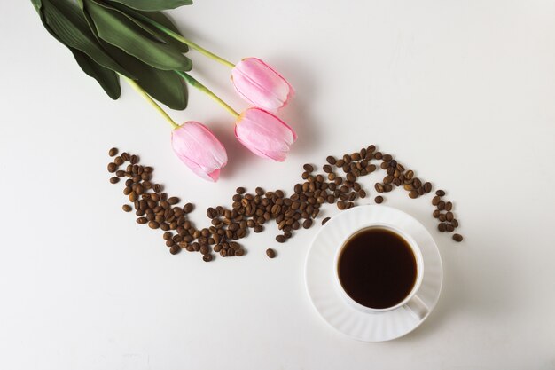 Witte kop met koffie, koffiebonen, tulpen op een wit oppervlak. Plat lag, bovenaanzicht