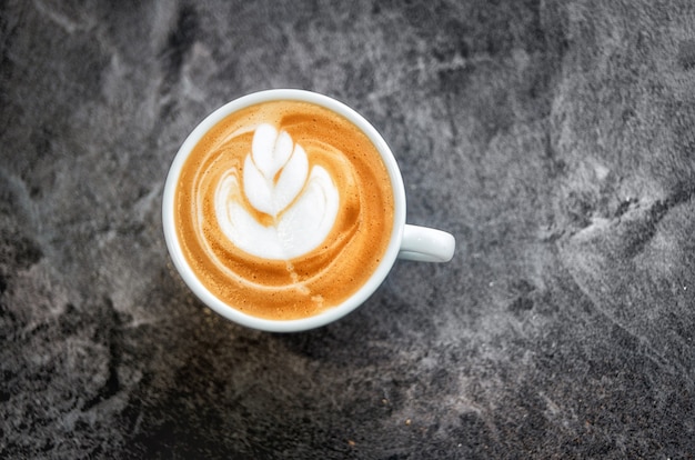 Witte kop met verse cappuccino met een prachtig patroon op het schuim op een donkere textuurtafel. Zachte ficus.