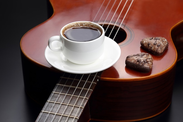 Witte kop met zwarte koffie en koekjes die op de akoestische gitaar liggen