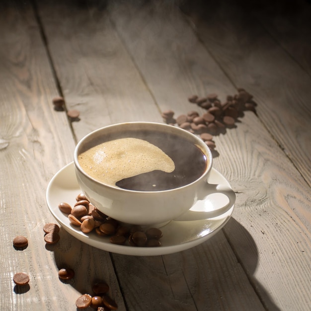 Witte kop warme koffie met stoom op een houten tafel met achtergrondverlichting