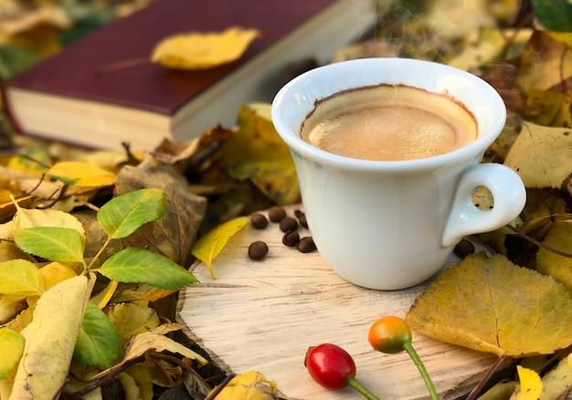 Witte kop warme koffie onder gevallen herfstbladeren