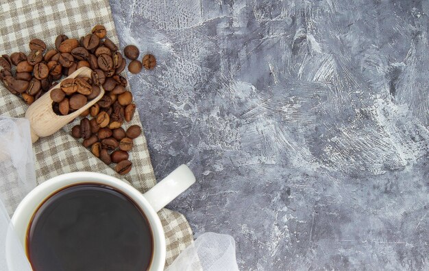 Witte kop zwarte koffie americano, stoffen sjaal met koffiebonen verspreid over een grijze tafel. Mooie kop compositie. Plat lag, bovenaanzicht, kopieer ruimte. Ontspanningsconcept.