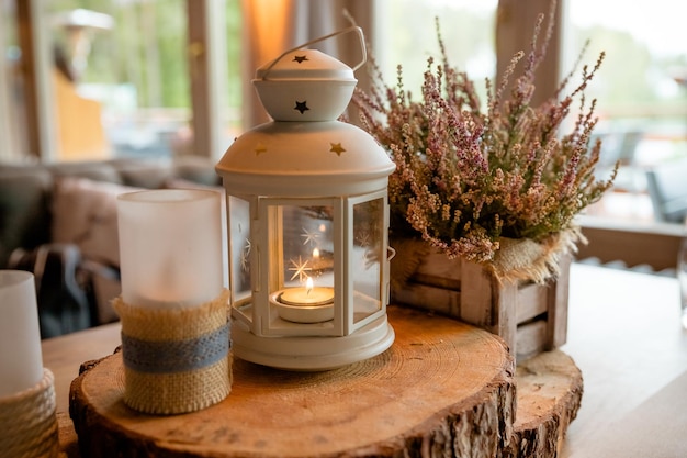 Witte lantaarn met brandende kaars erin staande op feestelijke tafel versierd op houten plak en bloemen op achtergrond Decor bruiloft Herfst stilleven getinte afbeelding roze heide