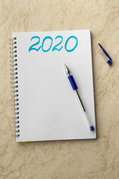 Witte laptop en de blauwe inscriptie 2020. Blauwe pen op papier en pet op een tafel