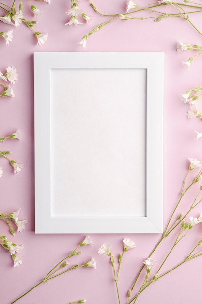 Witte lege fotolijst met muis-oor vogelmuur bloemen op roze tafel, bovenaanzicht kopie ruimte