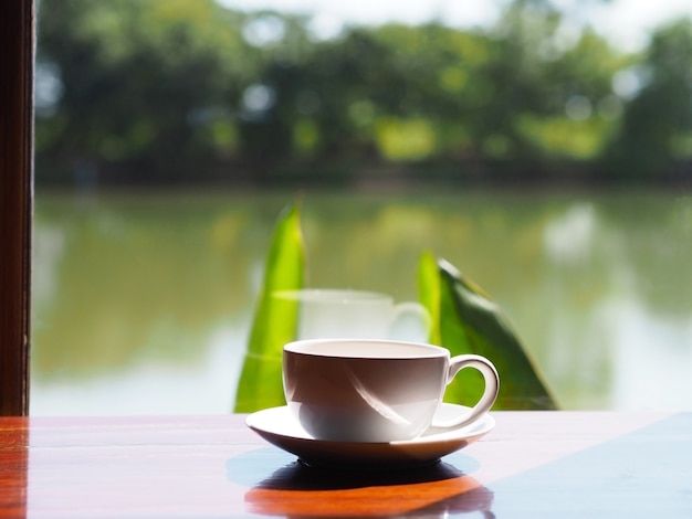 Witte lege kop koffie op houten tafel naast glasvenster