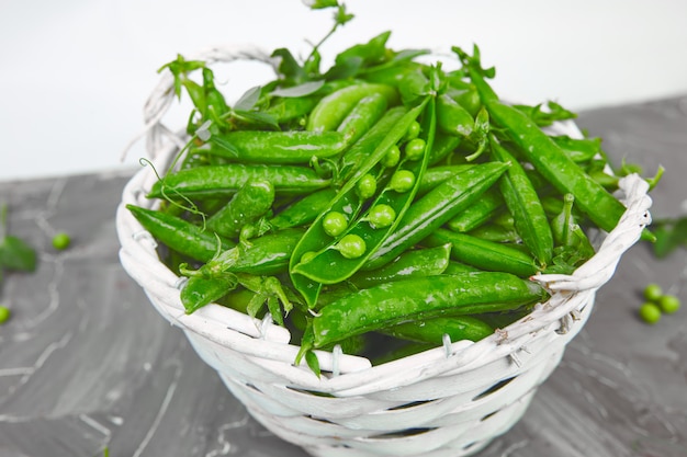 Witte mand met verse groene erwten op grijze tafel.