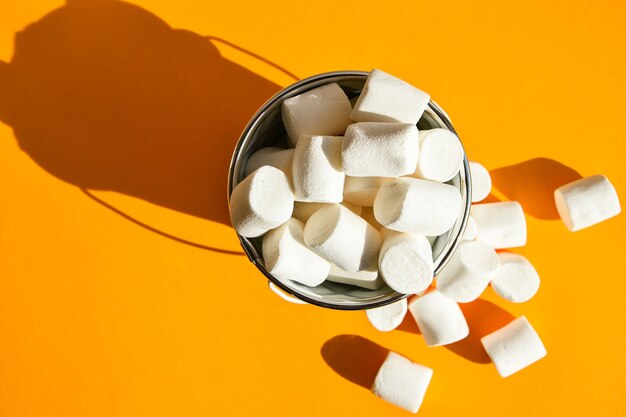 Witte marshmallows in een witmetalen emmer op een gele achtergrondkopieerruimte, een ingrediënt voor het maken van een kerstdrankje en het decoreren van taarten. junk ongezond voedsel.